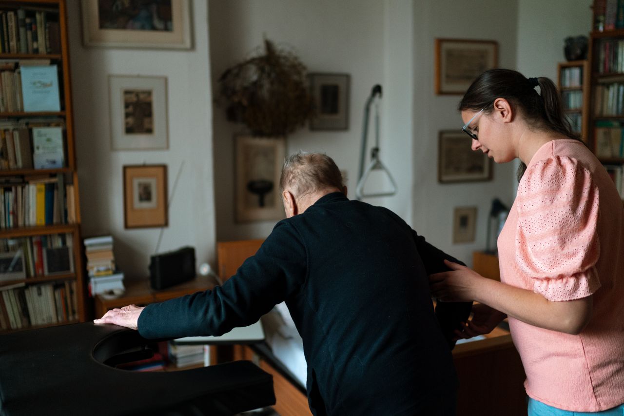 Services Young caregiver assisting senior man in a stylish Prague living room.