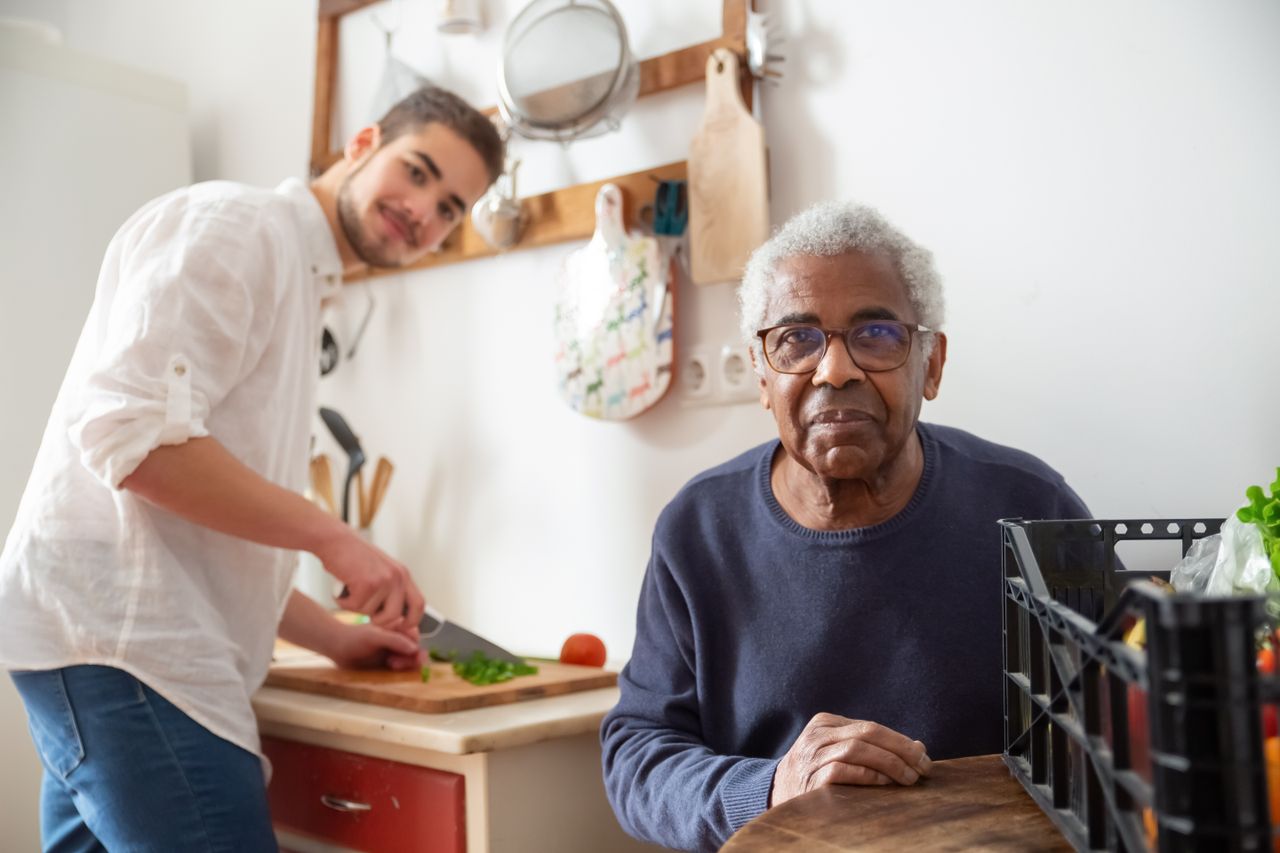 Services A young adult helping a senior in the kitchen, highlighting care and support at home.