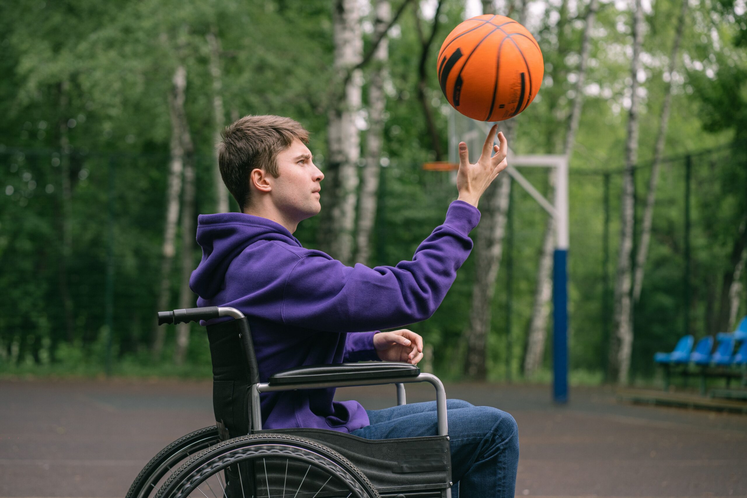 Home A man in a wheelchair skillfully spinning a basketball on his finger outdoors.